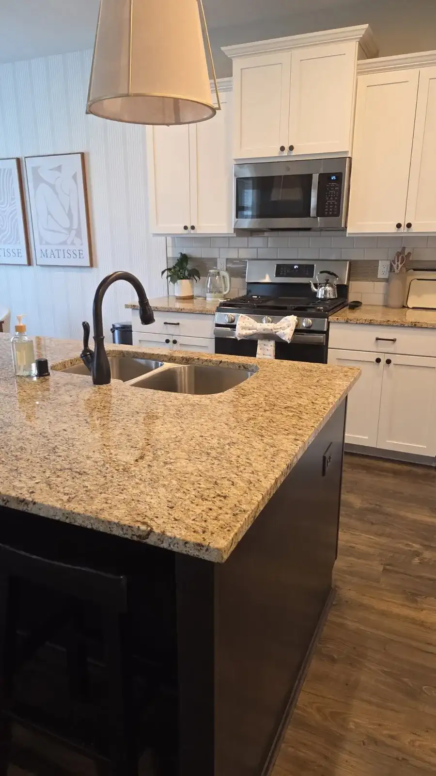 Clean white kitchen with a granite island, a shining sink and a towel tied in a bow on the oven