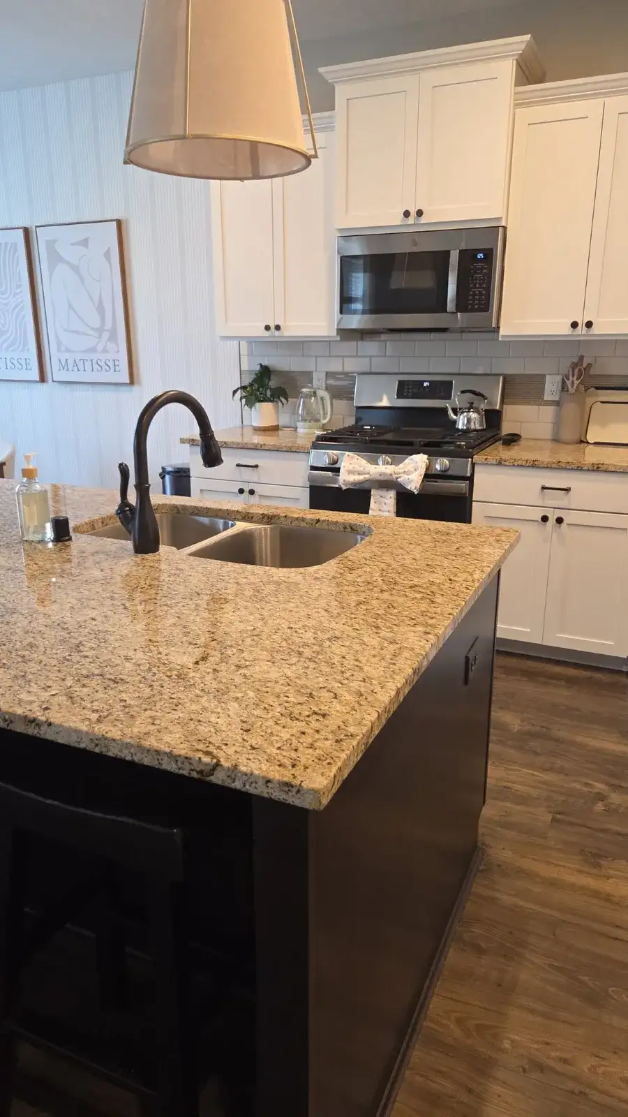 Clean white kitchen with a granite island, a shining sink and a towel tied in a bow on the oven