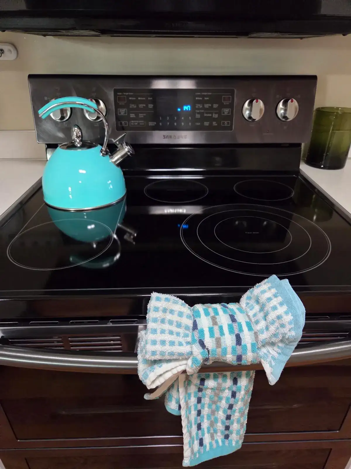 Clean glass-top range with a teal kettle and a towel tied in a bow on the handle